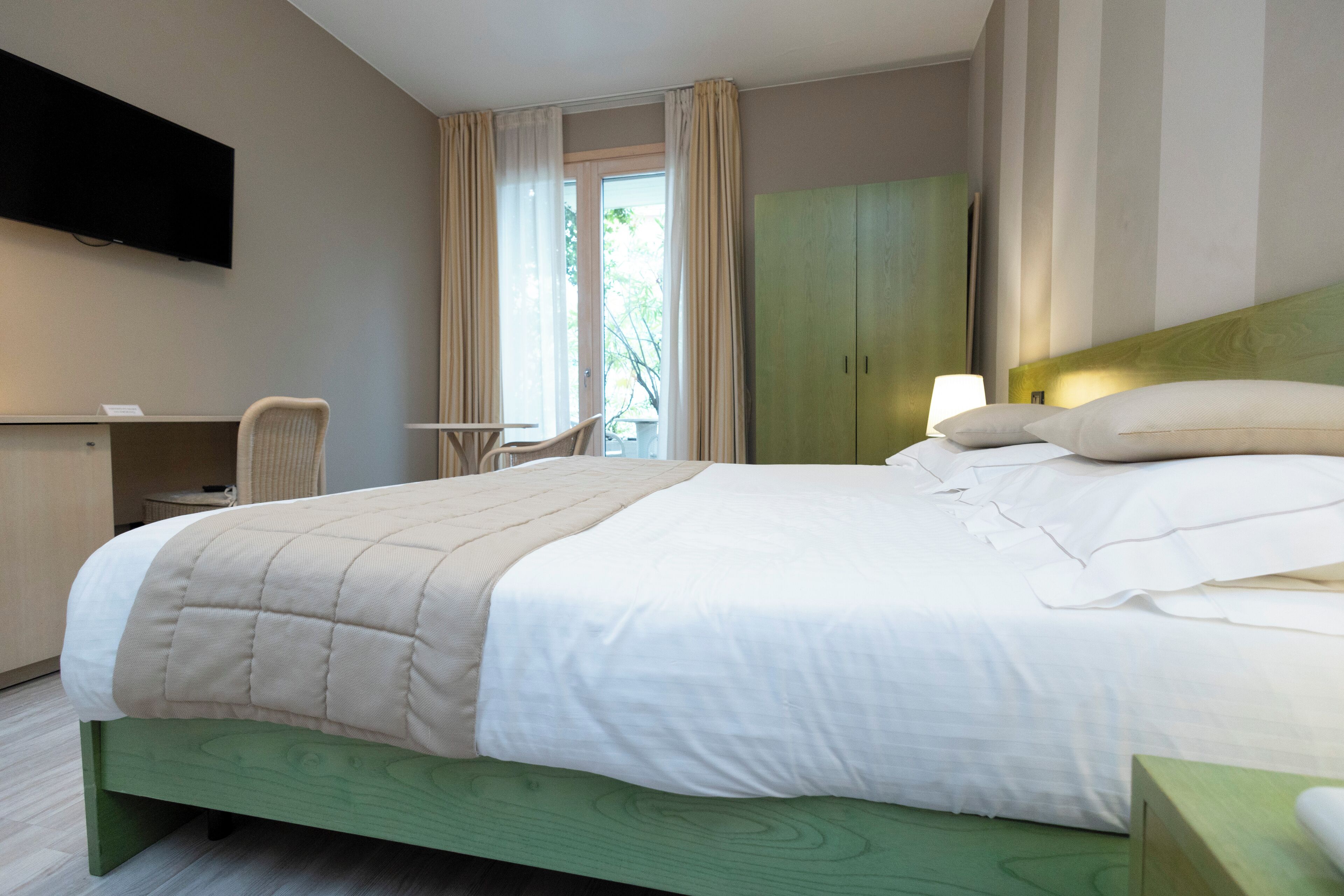 A hotel room with a bed, a desk, a chair, a TV, and a wardrobe.