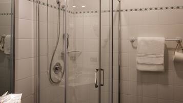 Una cabina doccia in vetro con soffione a mano, un portasciugamani con un asciugamano bianco e un cesto di articoli da toilette sul lavandino.