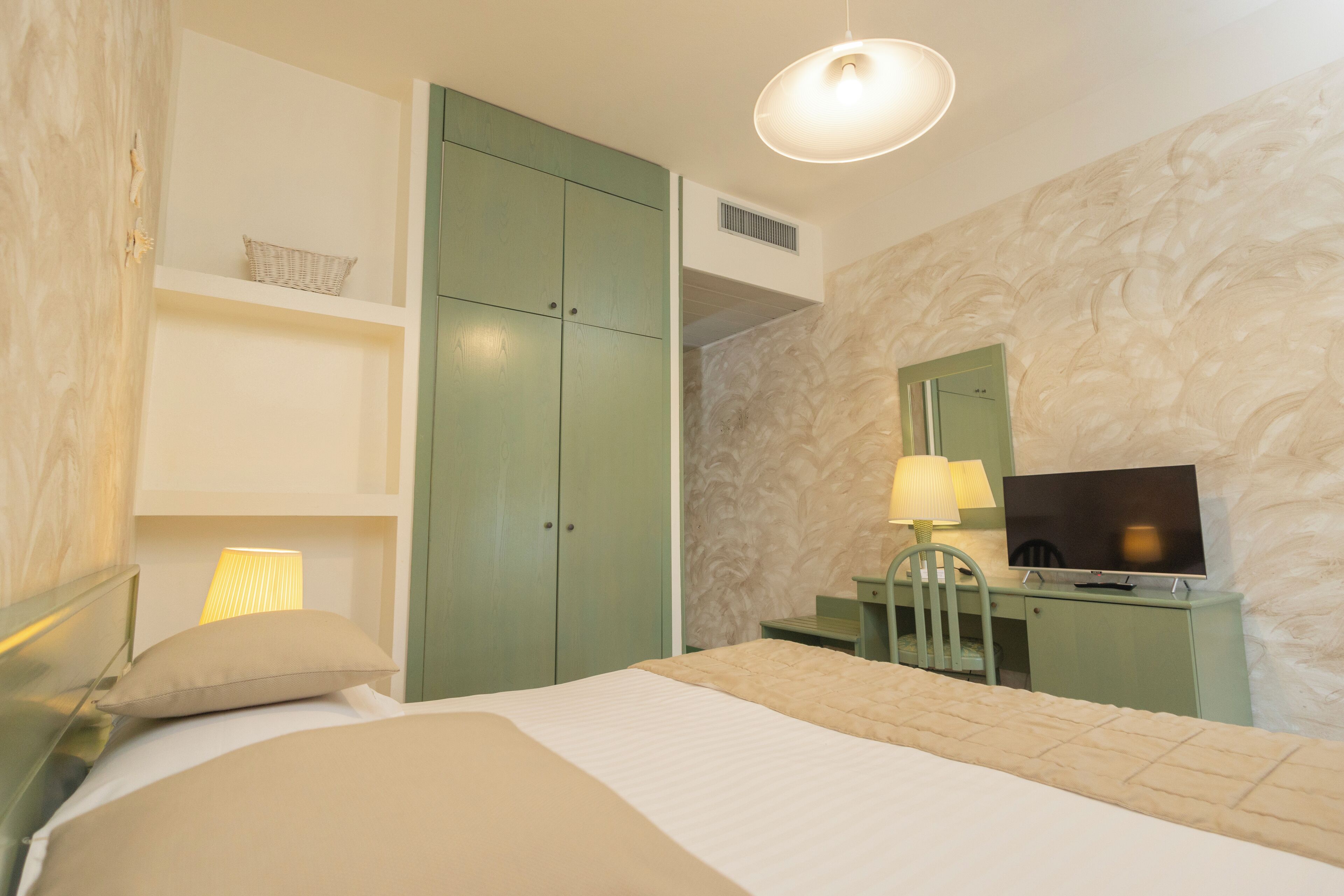 Une chambre à coucher avec un lit, un bureau et une chaise, une télévision et une lampe.
