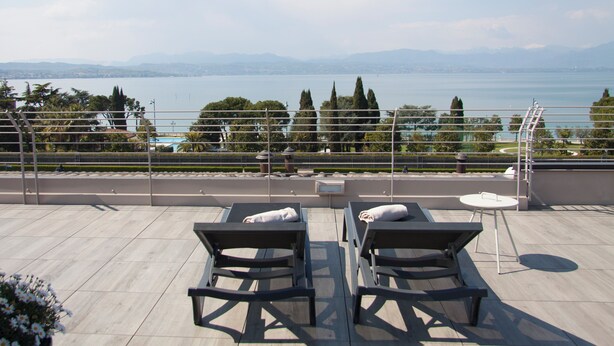 A rooftop terrace with two lounge chairs, a small table, and a view of a lake and mountains. - Hotel Berta (Desenzano del Garda)