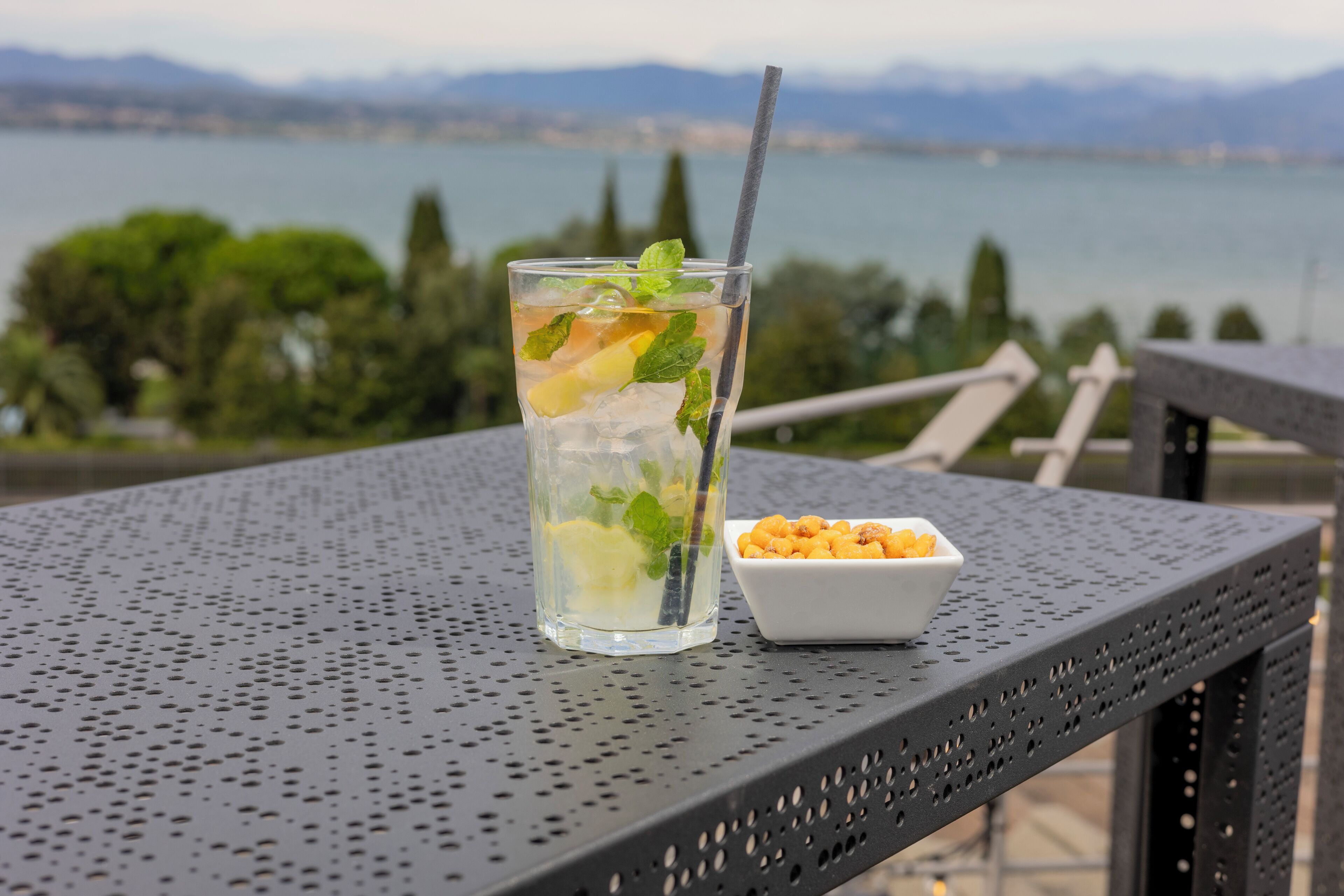 Un verre de boisson fraîche, à la menthe et au citron, posé sur une table en métal, avec une vue panoramique en arrière-plan.
