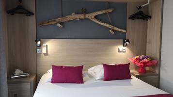 Een moderne slaapkamer met een houten hoofdbord, twee witte kussens, twee rode kussens, een nachtkastje met een lamp en een wandlamp.