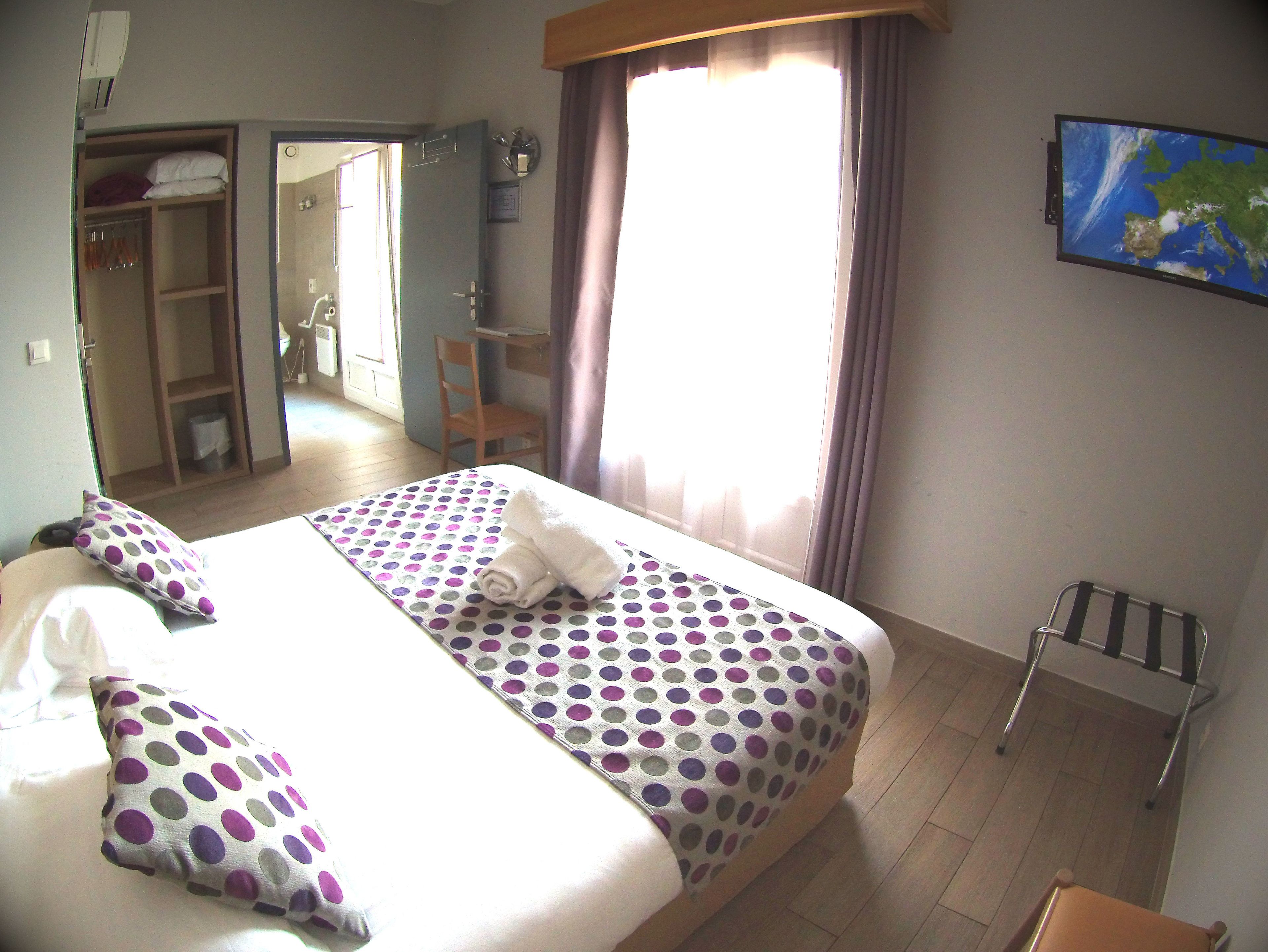 A hotel room with a bed, a chair, a desk, and a map on the wall.