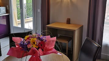 Une pièce moderne avec une table ronde en bois, un bouquet de fleurs, une petite table d’appoint en bois, une chaise noire et un luminaire décoratif.