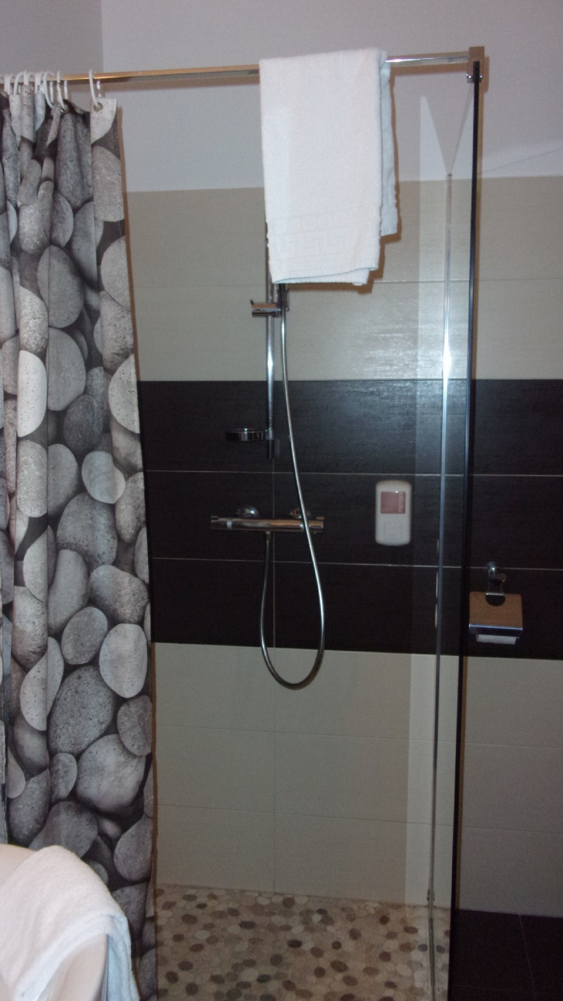 A shower with a glass door, a towel hanging on the door, and a tiled wall with a pebble pattern.