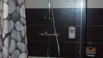A shower with a glass door, a towel hanging on the door, and a tiled wall with a pebble pattern.