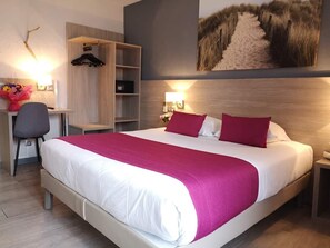 A hotel room with a large bed, a desk with a chair, a wardrobe, and a wall-mounted TV.