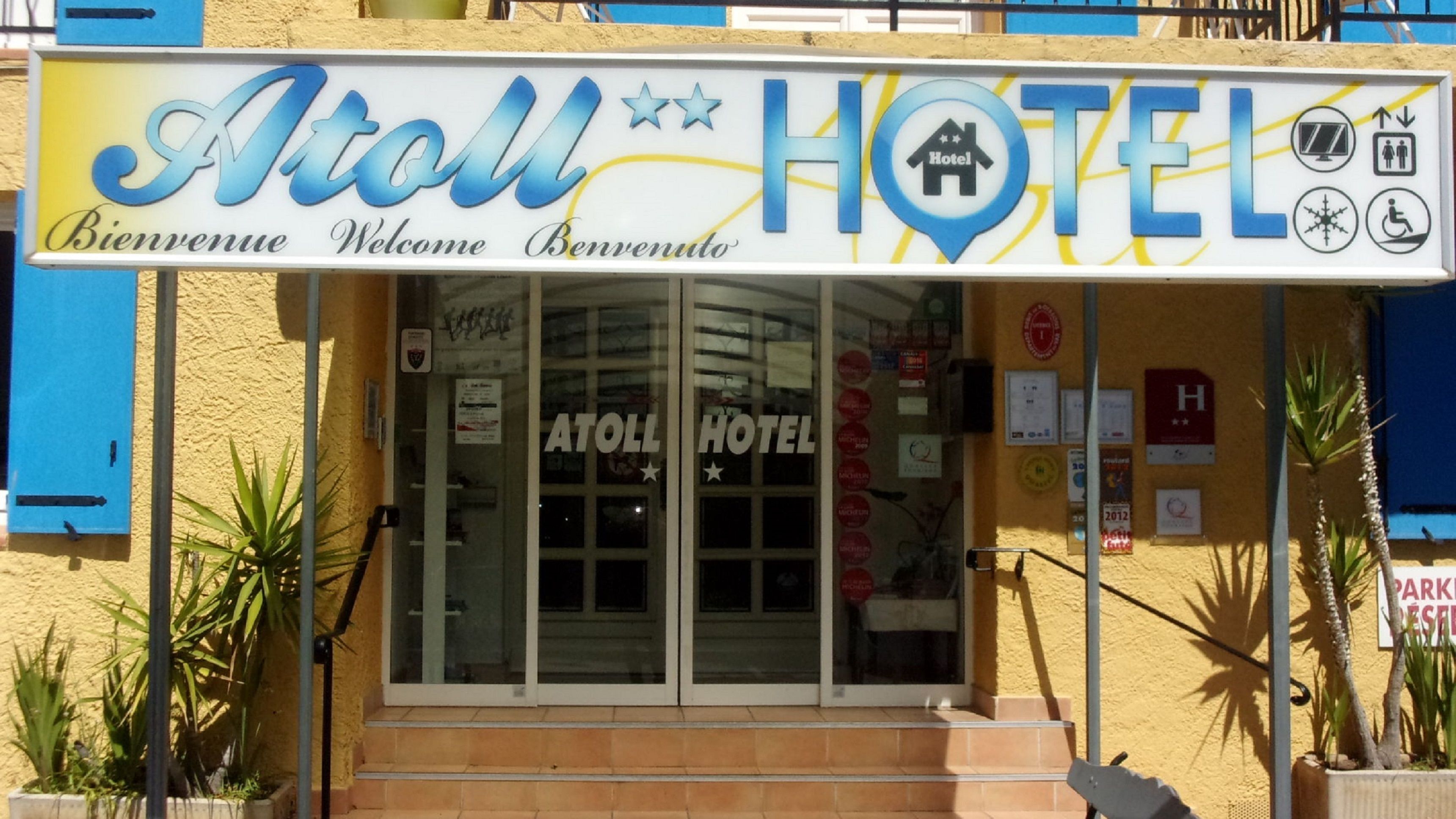 Entrada de un hotel con un cartel que dice "Atoll Hotel" y "Bienvenue Welcome Benvenuto".