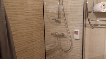 A glass-enclosed shower with a handheld showerhead, a wall-mounted towel rack, and a control panel.