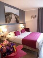 Habitación de hotel con una cama, una mesita de noche con lámpara, un cuadro en la pared y un arreglo floral.