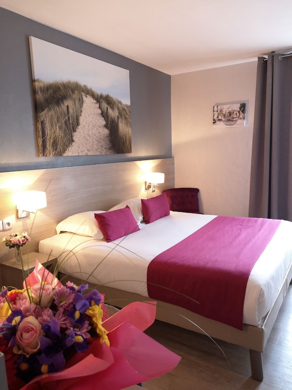 A hotel room with a bed, a nightstand with a lamp, a wall-mounted picture, and a floral arrangement.