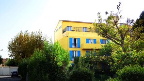 A yellow building with blue shutters and balconies, surrounded by greenery.
