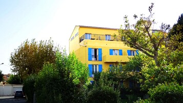 Un edificio amarillo con contraventanas azules y balcones, rodeado de follaje.