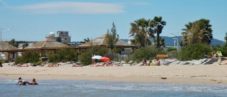 A beach with people sunbathing, umbrellas, and palm trees.
