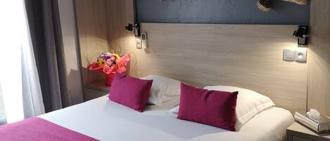Una cama bien hecha con una colcha blanca y rosada, un cabecero de madera y una rama decorativa colgando arriba.