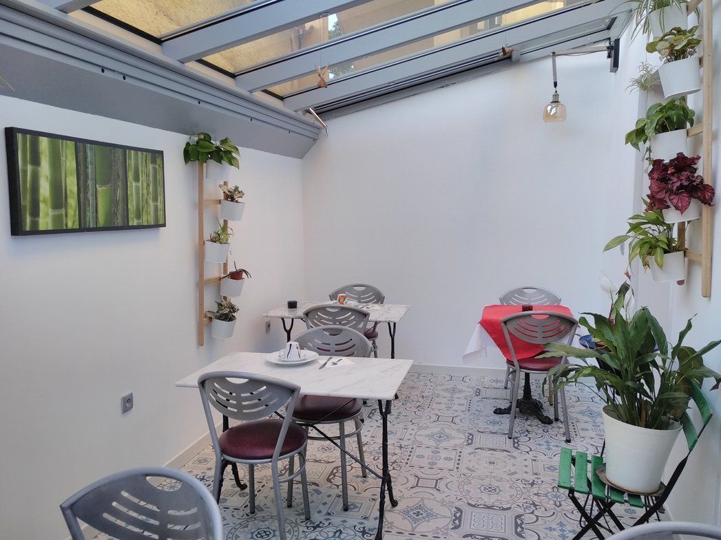 Un área de comedor con mesas y sillas, una estantería para plantas en la pared y un tragaluz.