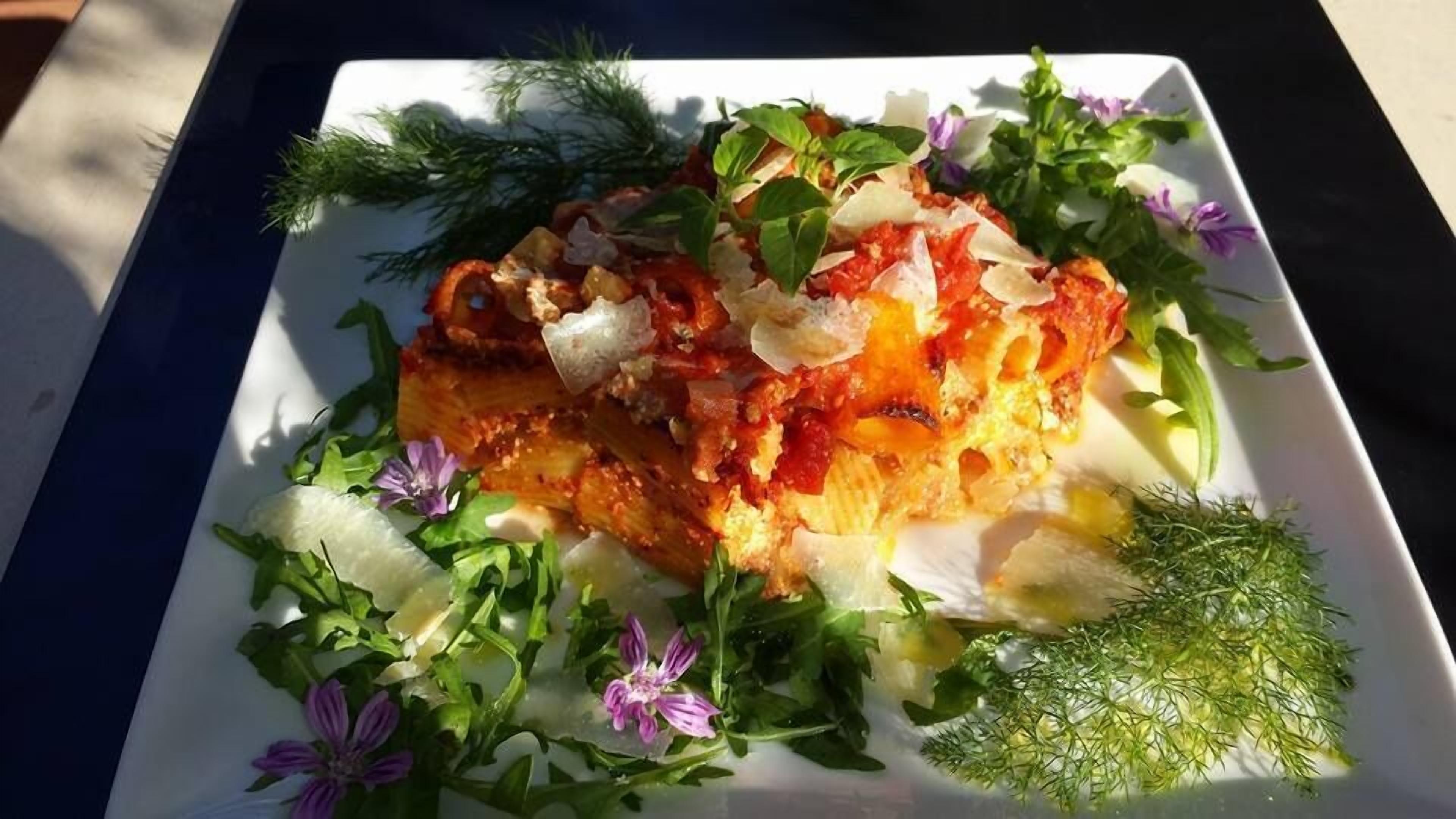 A square plate with a dish garnished with herbs and flowers, placed on a table.