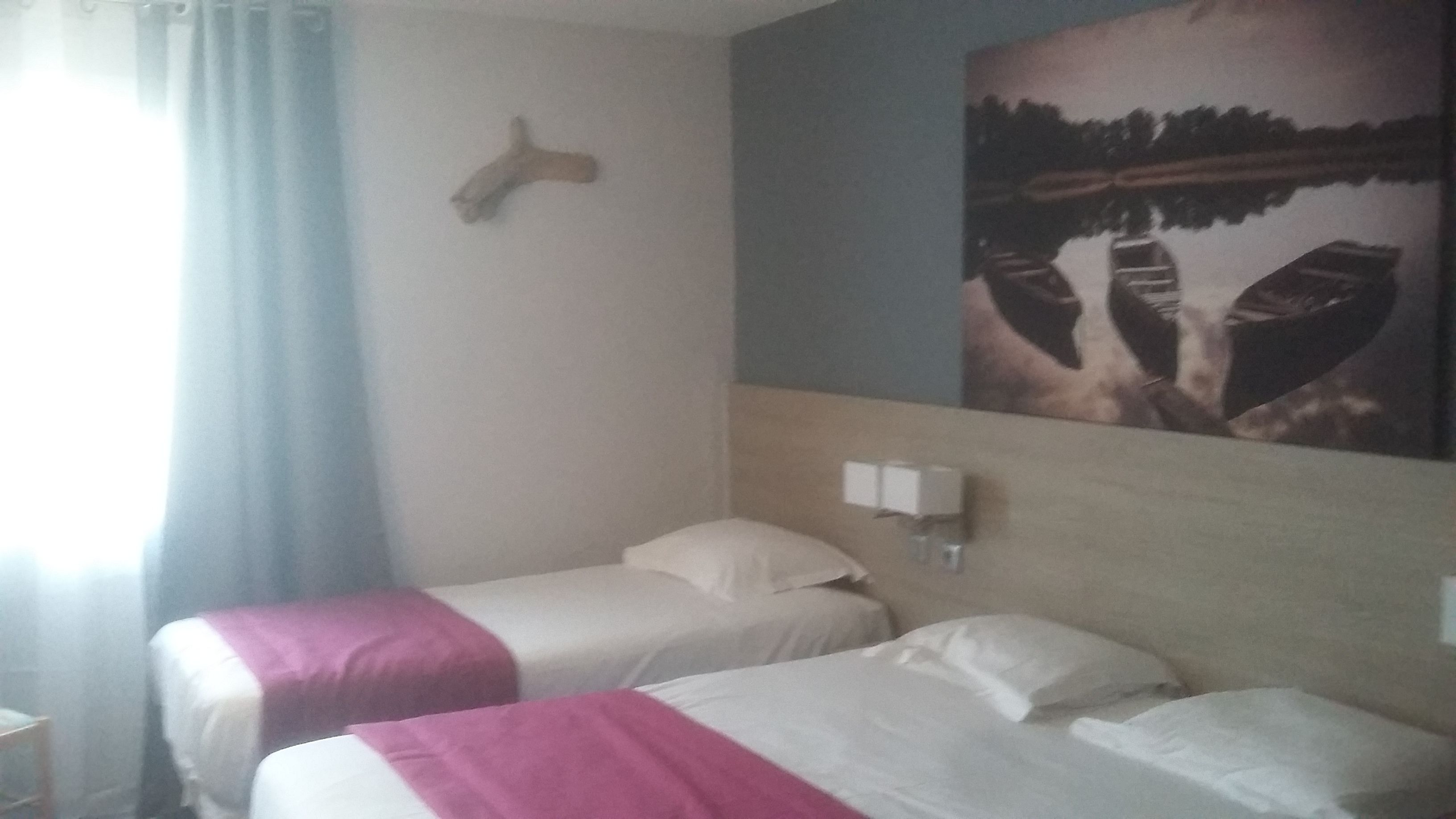 A hotel room with two beds, a painting of a landscape, and a wooden headboard.
