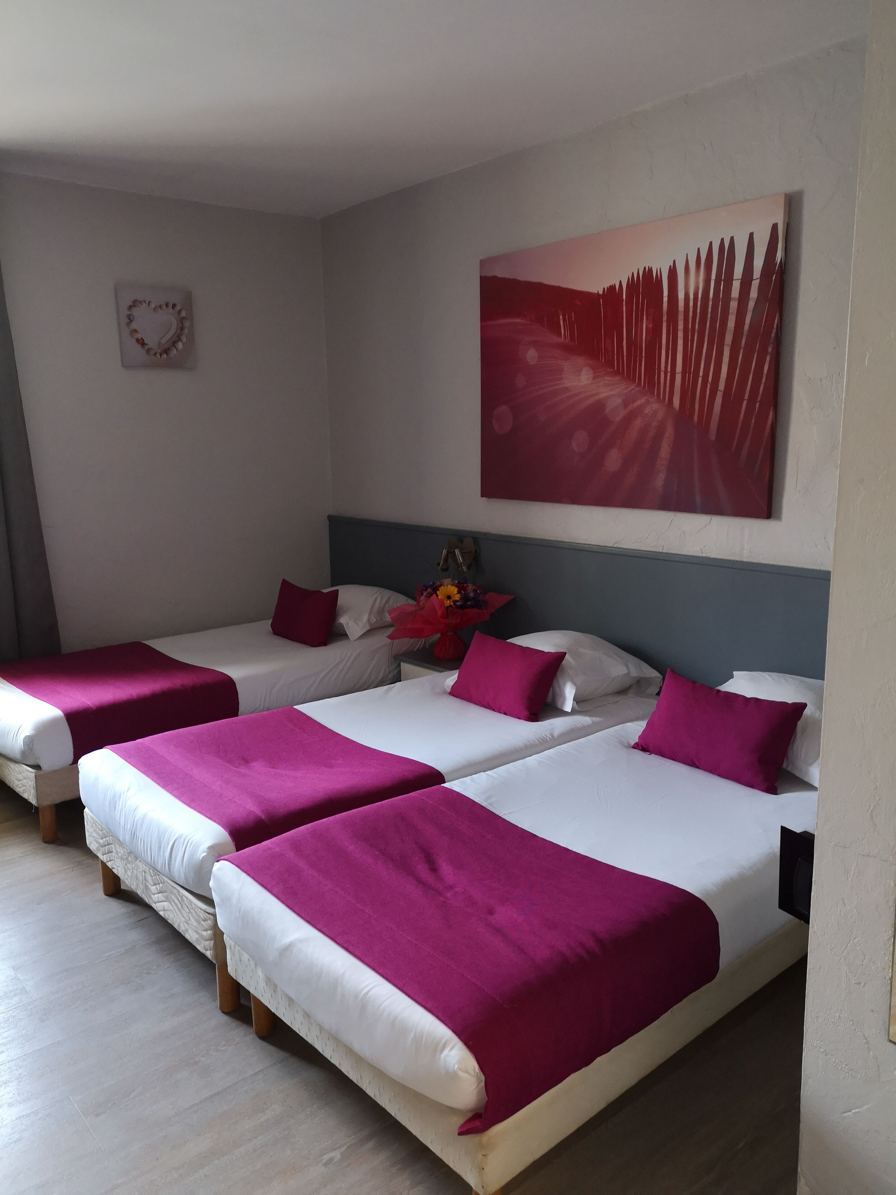 Een hotelkamer met drie bedden, elk voorzien van beddengoed in wit en roze. Daarboven hangt een groot schilderij aan de muur.