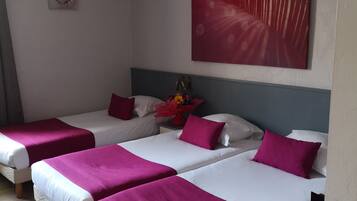 Habitación de hotel con tres camas, cada una con ropa de cama blanca y rosa. Encima de las camas, hay un cuadro grande en la pared.