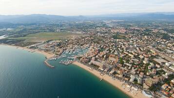 Vista aerea di una città costiera con un porto turistico, un'area urbana densa e campi verdi circostanti.