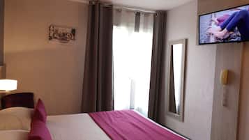 A hotel room with a bed, a television, a window with curtains, and a wall-mounted picture.