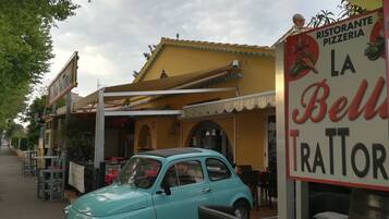 A vintage turquoise car parked in front of a restaurant named "La Bella Trattoria."