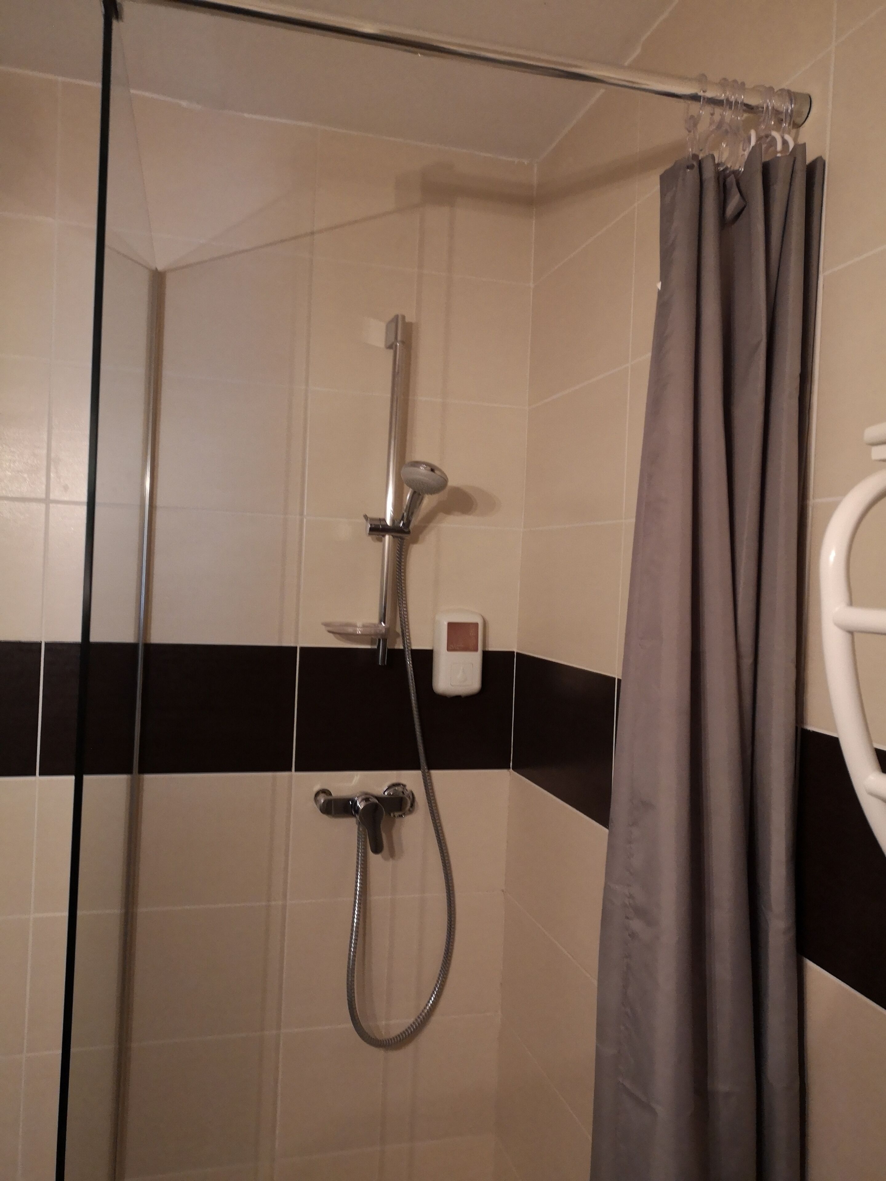 Un espacio de ducha con mampara de vidrio, un cabezal de ducha manual, un panel de control en la pared y una cortina gris.