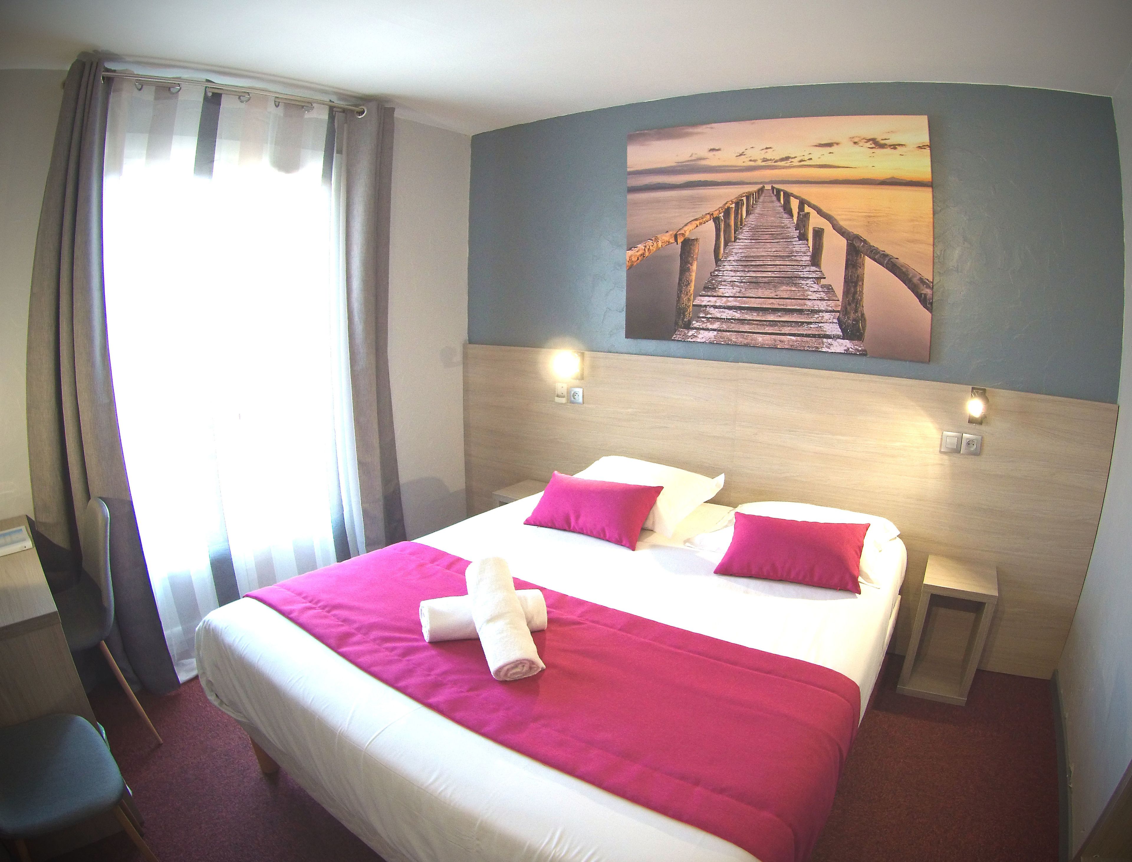 A hotel room with a bed, two bedside tables, a headboard, a painting of a pier, and a window with curtains.