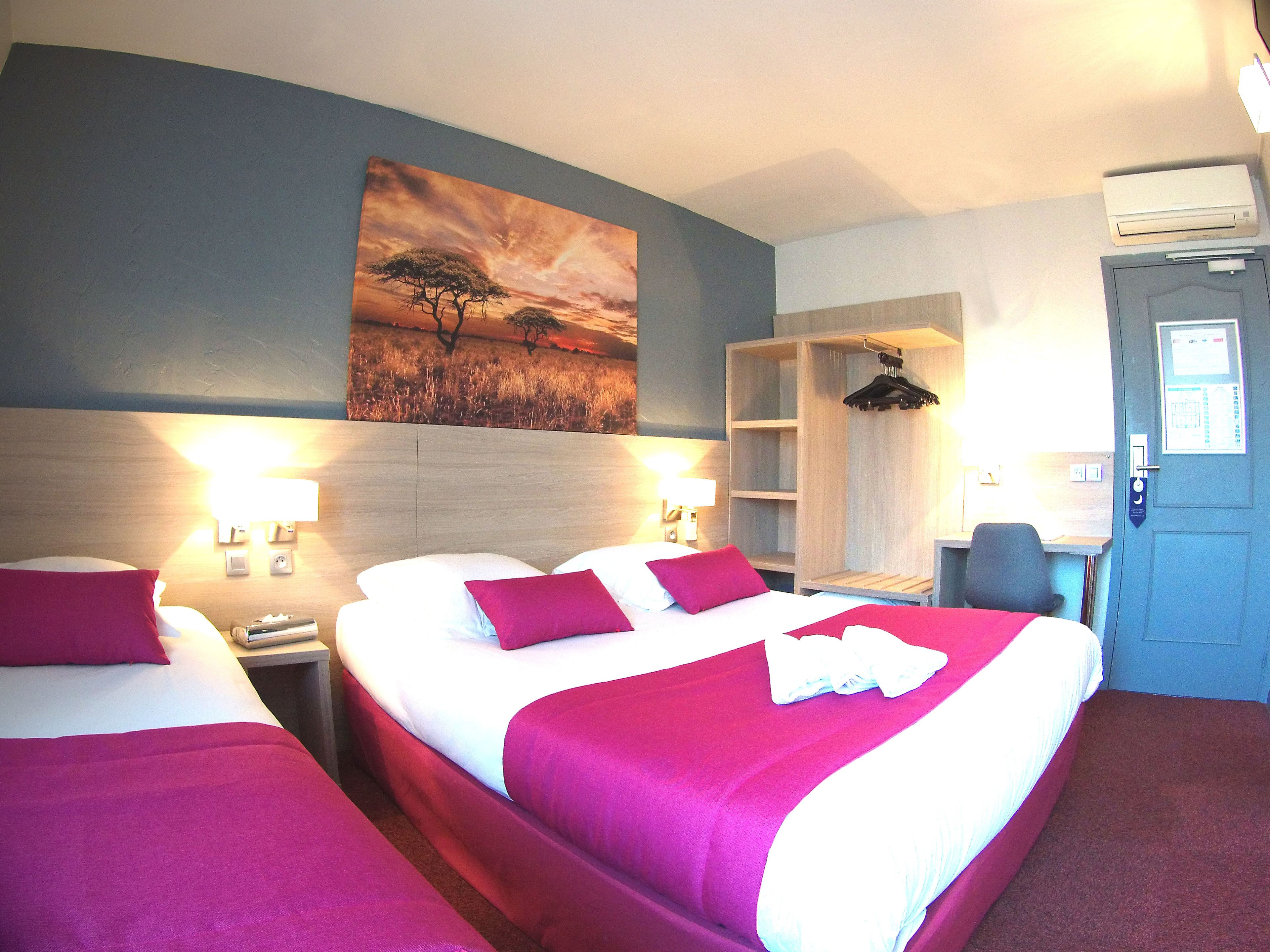 A hotel room with two beds, a painting of a sunset, a desk with a chair, and a wardrobe.