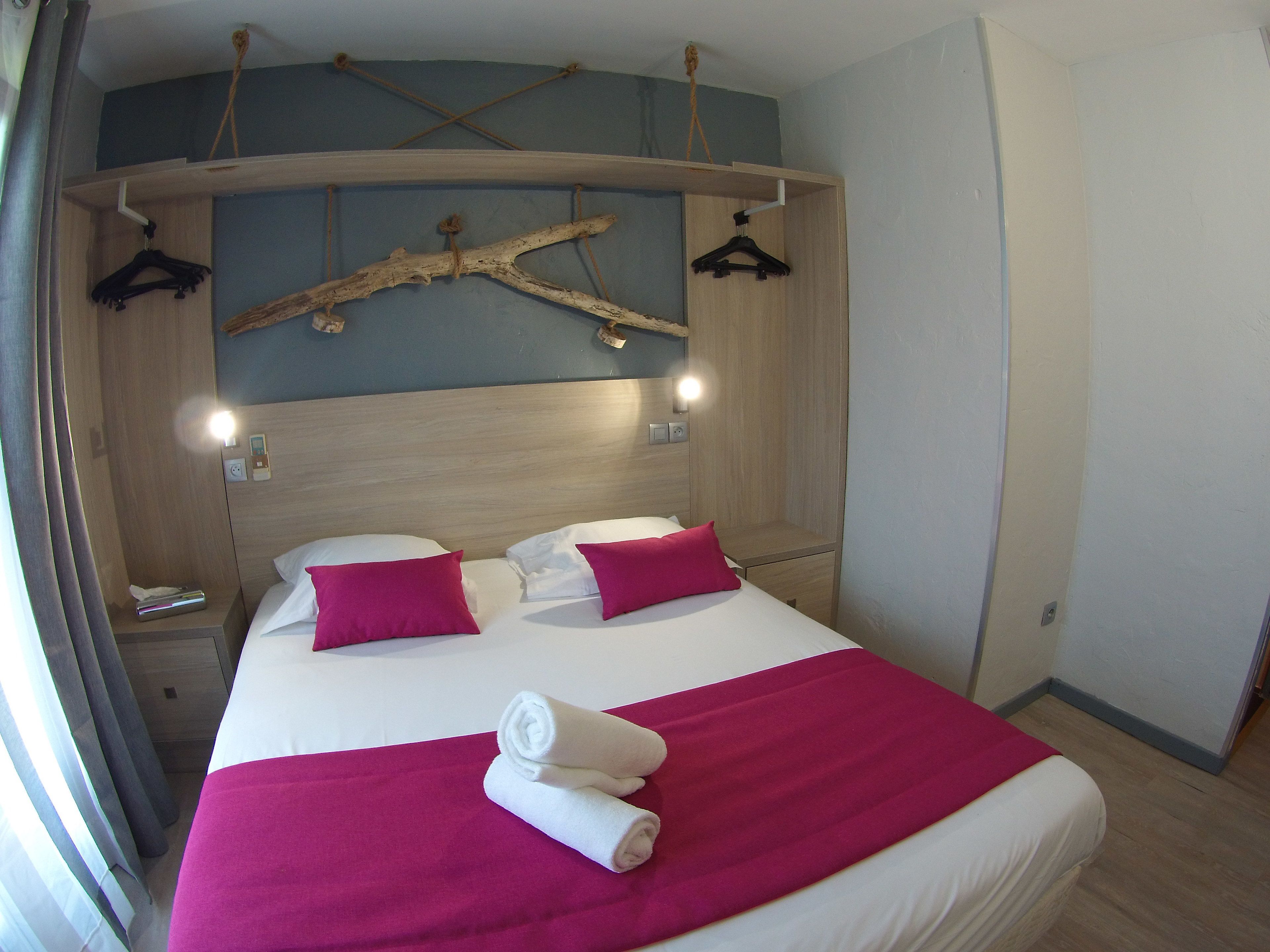 Hotelkamer met een bed, twee kussens, een hoofdbord, een nachtkastje, een lamp en een raam met gordijnen.
