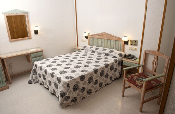 Un dormitorio con cama, mesita de noche, silla y espejo en la pared.