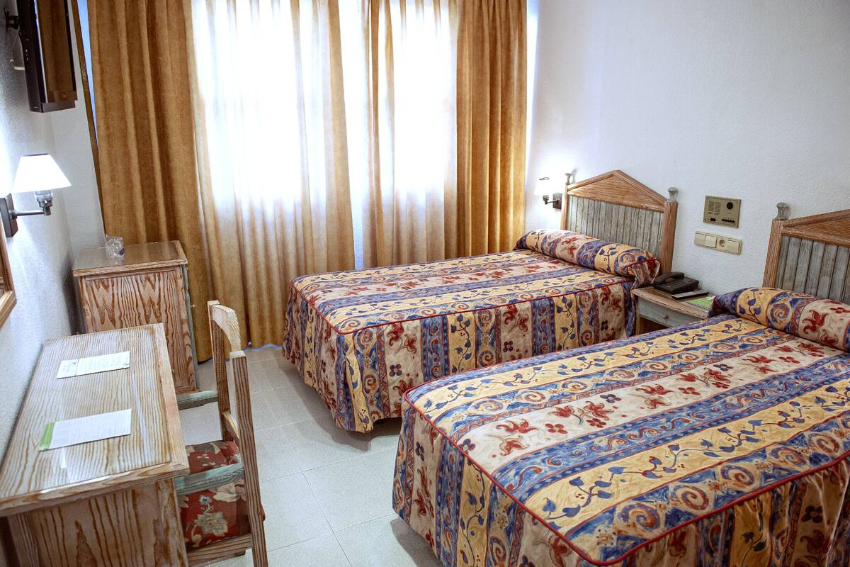 Una habitación de hotel con dos camas, un escritorio de madera, una silla y una mesita.