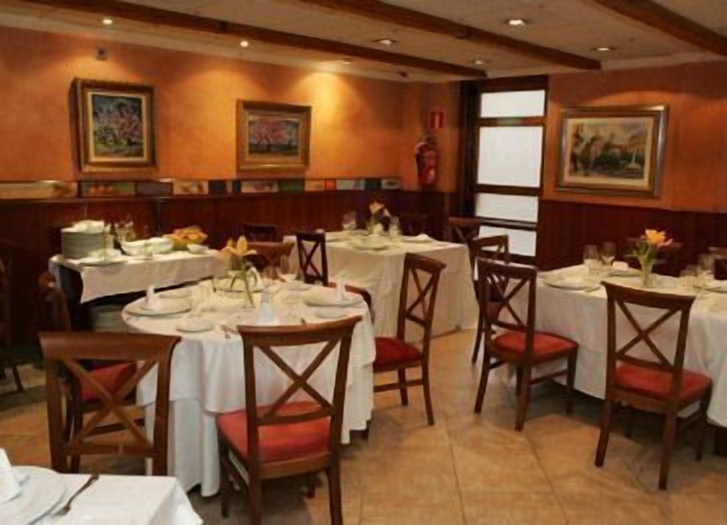 Un restaurante con mesas redondas, sillas de madera y cuadros en las paredes.