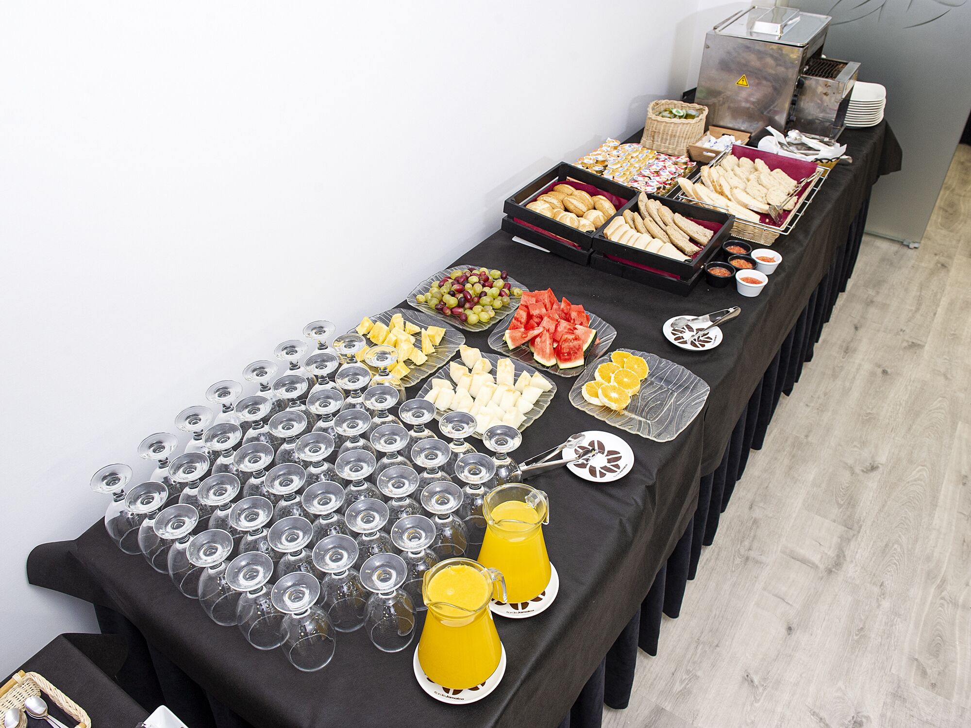 Une table de buffet proposant une variété de plats et de boissons, notamment des fruits, des pâtisseries et un distributeur de jus.
