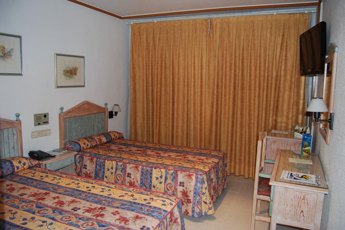 Habitación de hotel con dos camas, un escritorio, una silla, un televisor y una ventana con cortinas.