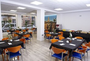 Un restaurante con varias mesas y sillas, vista a coches estacionados afuera y un mural en la pared.