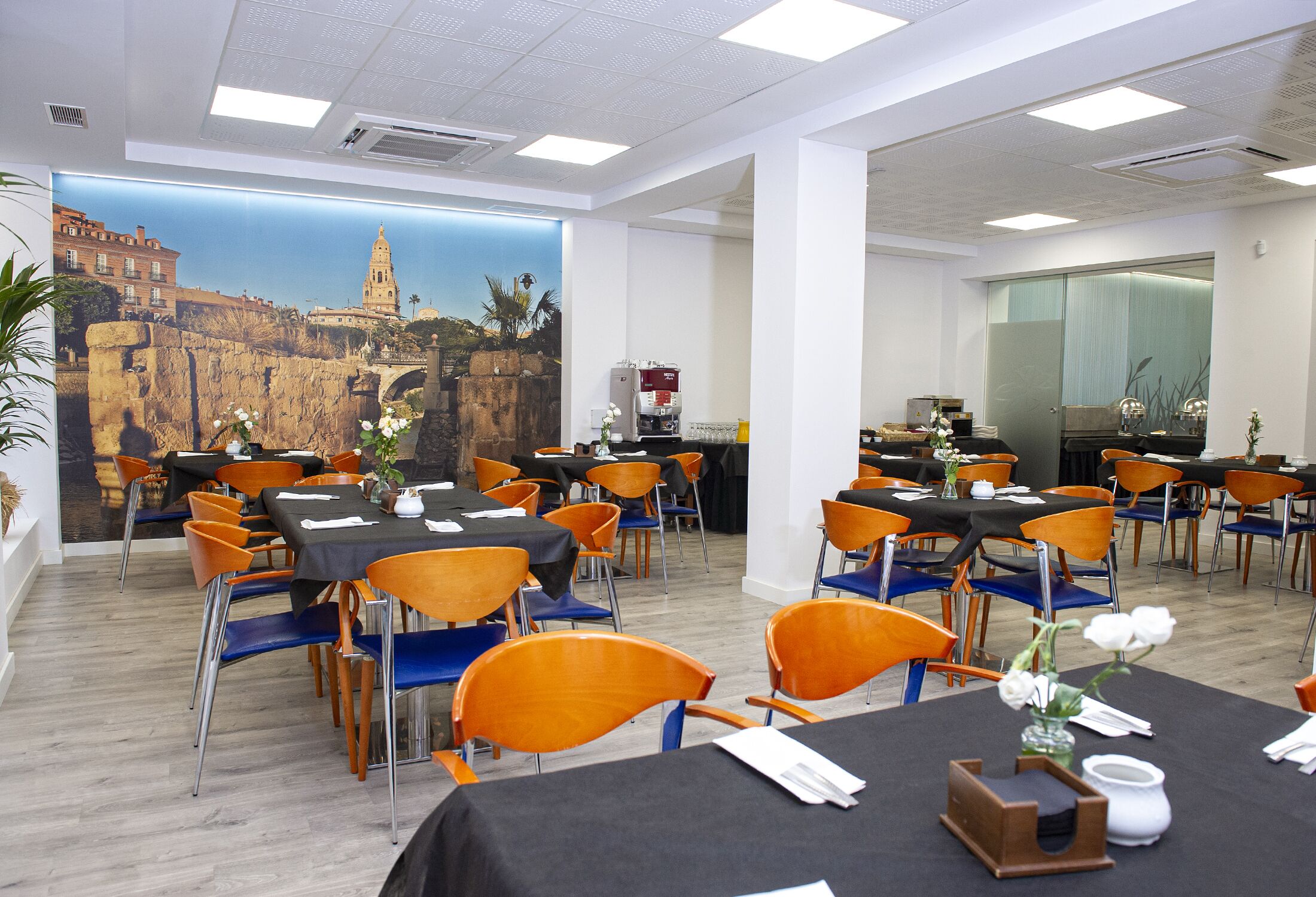 A dining area with tables and chairs, a mural of a cityscape, and a coffee machine.
