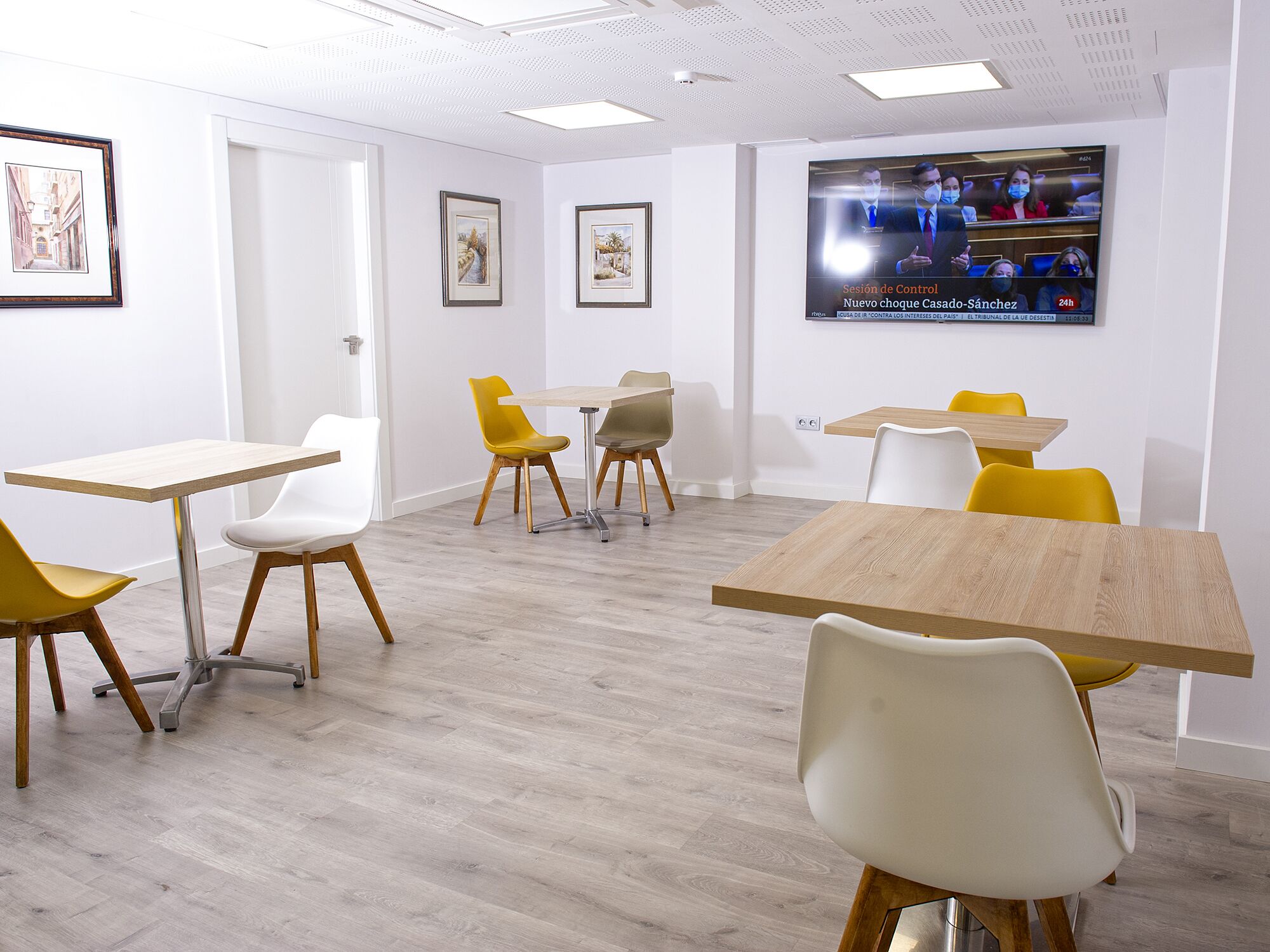 Une salle de conférence aux murs blancs, au sol en bois, et dotée de chaises jaunes et blanches disposées autour de tables.