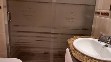 A bathroom with a glass shower enclosure, a toilet, and a sink with a granite countertop.