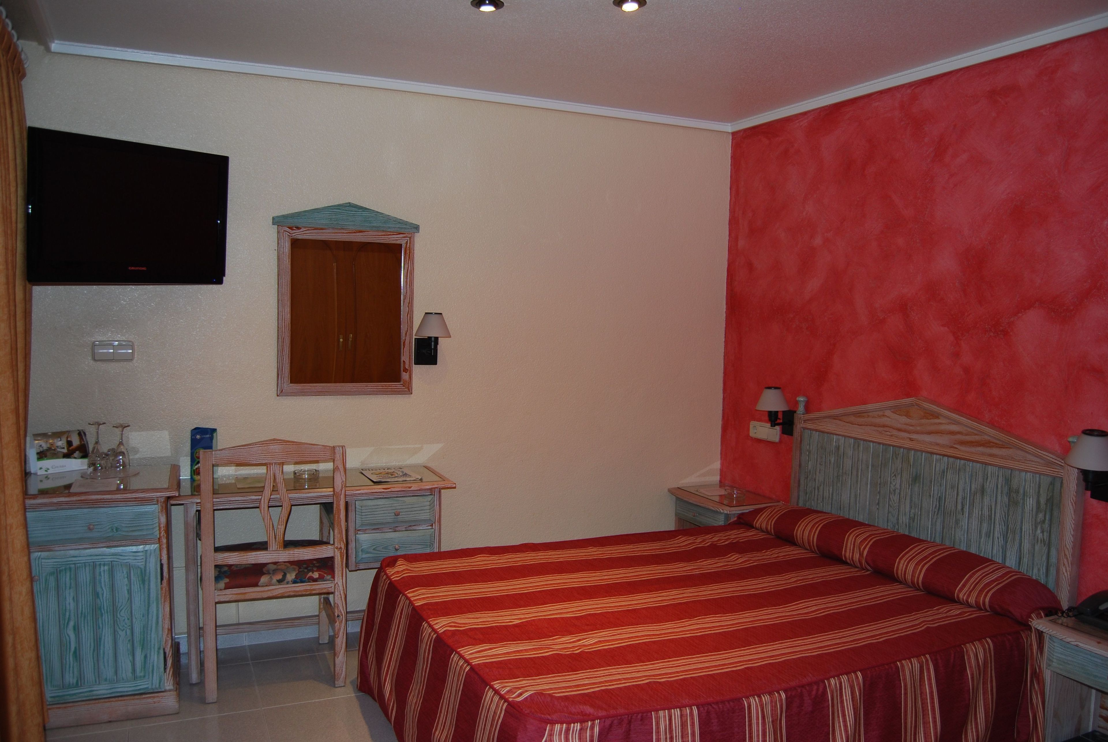 Un dormitorio con cama, un escritorio con silla, televisor y armario.