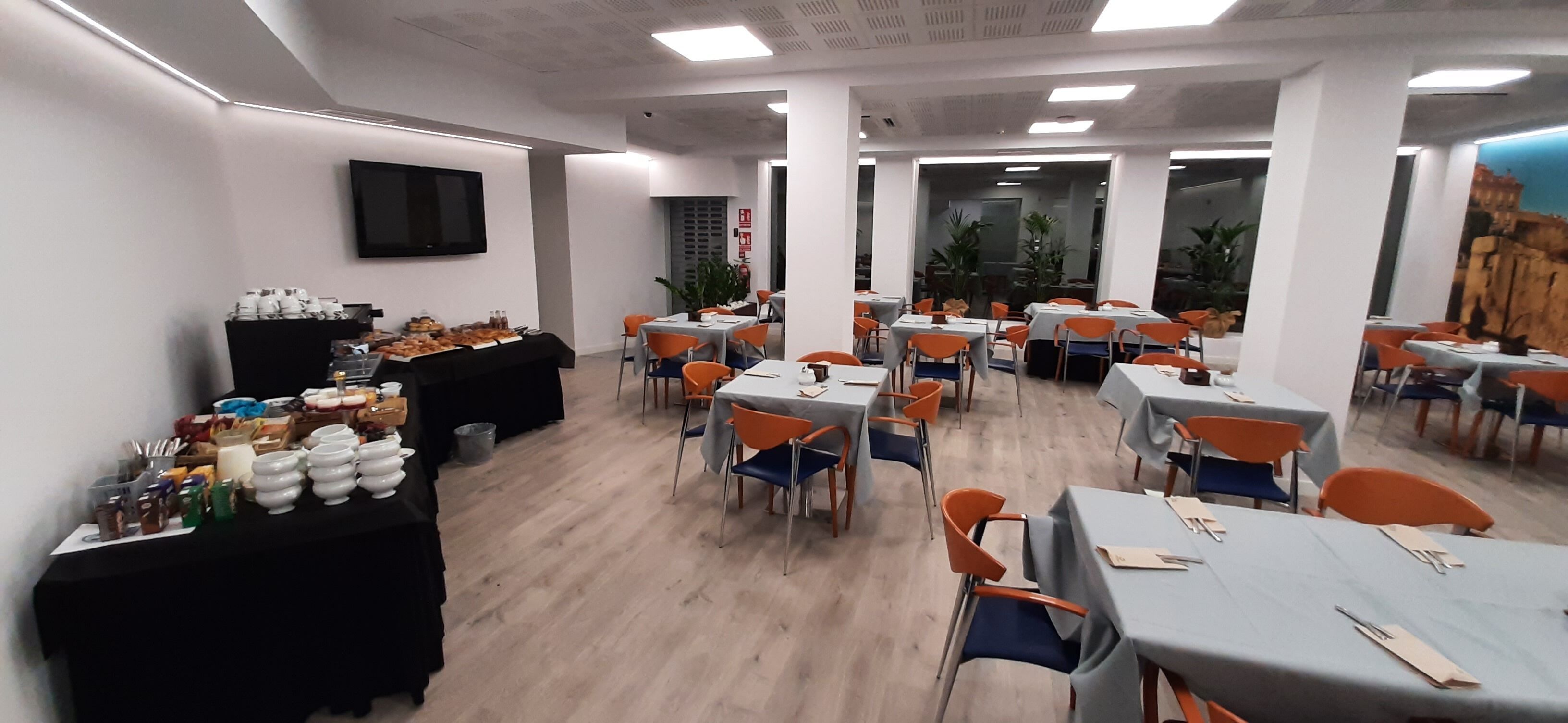 Een ruime eethoek met meerdere tafels en stoelen, een flatscreen televisie aan de muur en een buffet met diverse gerechten.