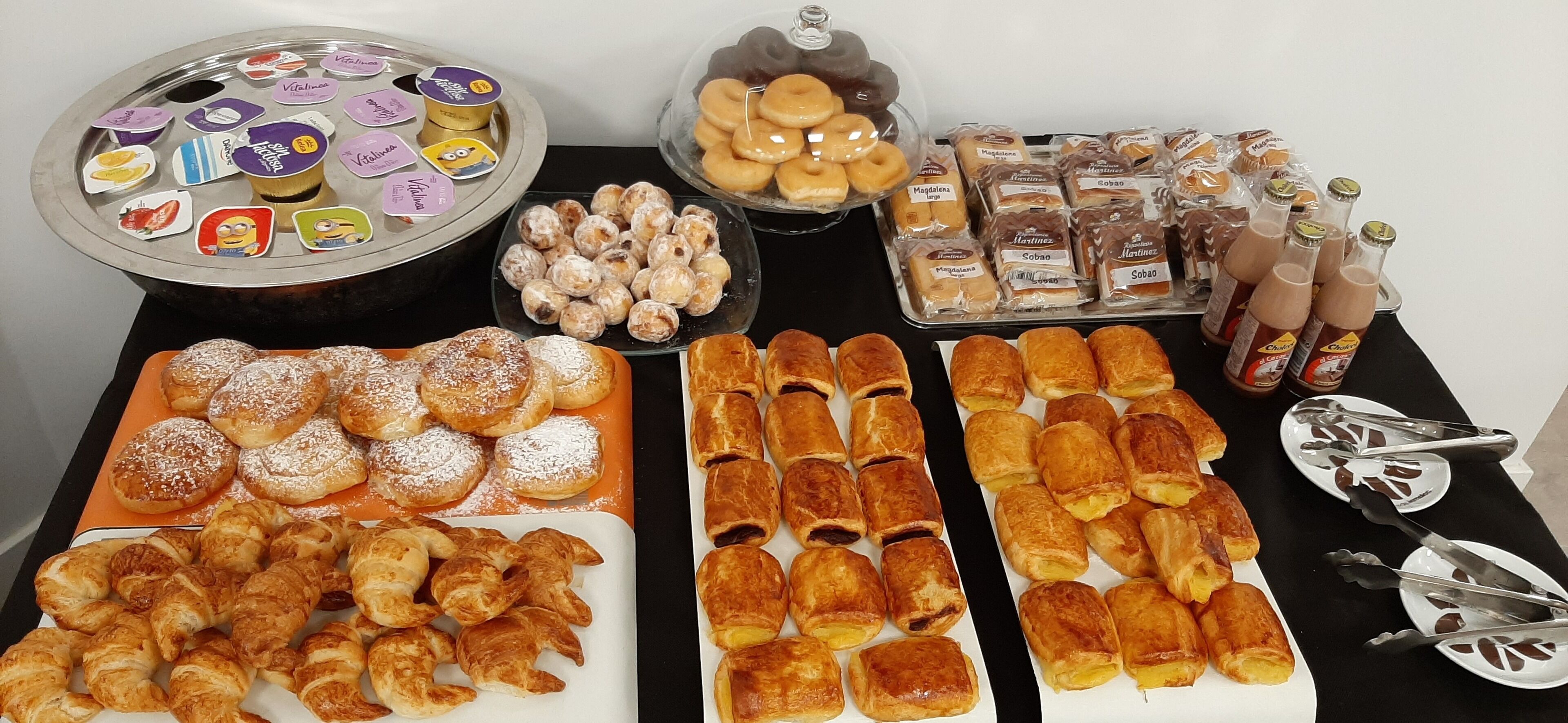 A buffet table with various pastries, including croissants, danishes, and cookies, as well as bottles of beverages.