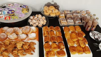A buffet table with various pastries, including croissants, danishes, and cookies, as well as bottles of beverages.