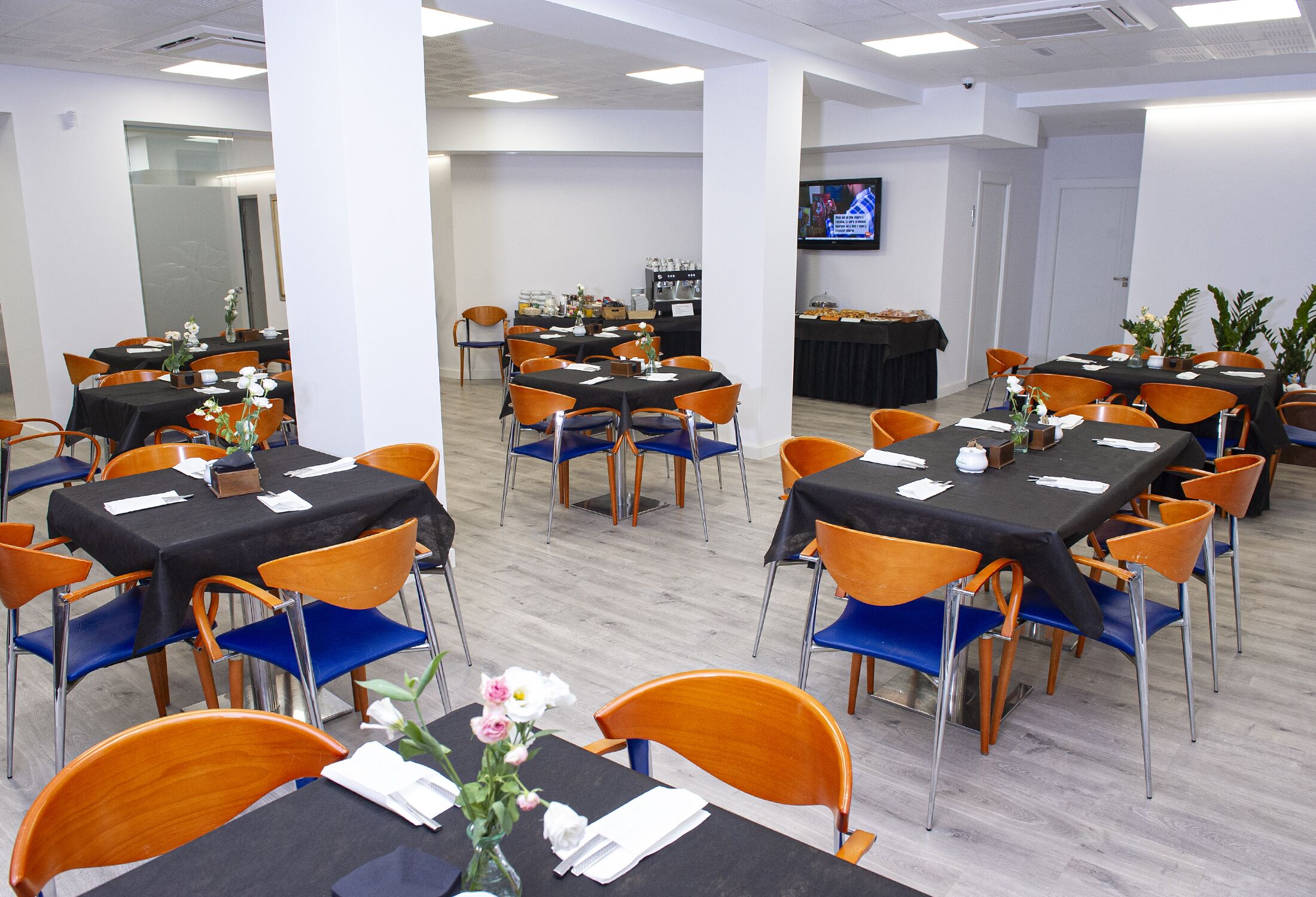 A conference room with multiple tables and chairs, a television screen, and a buffet area.