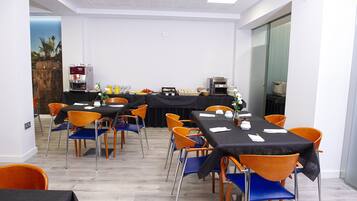A conference room with multiple tables and chairs, equipped with a coffee machine and a toaster oven.
