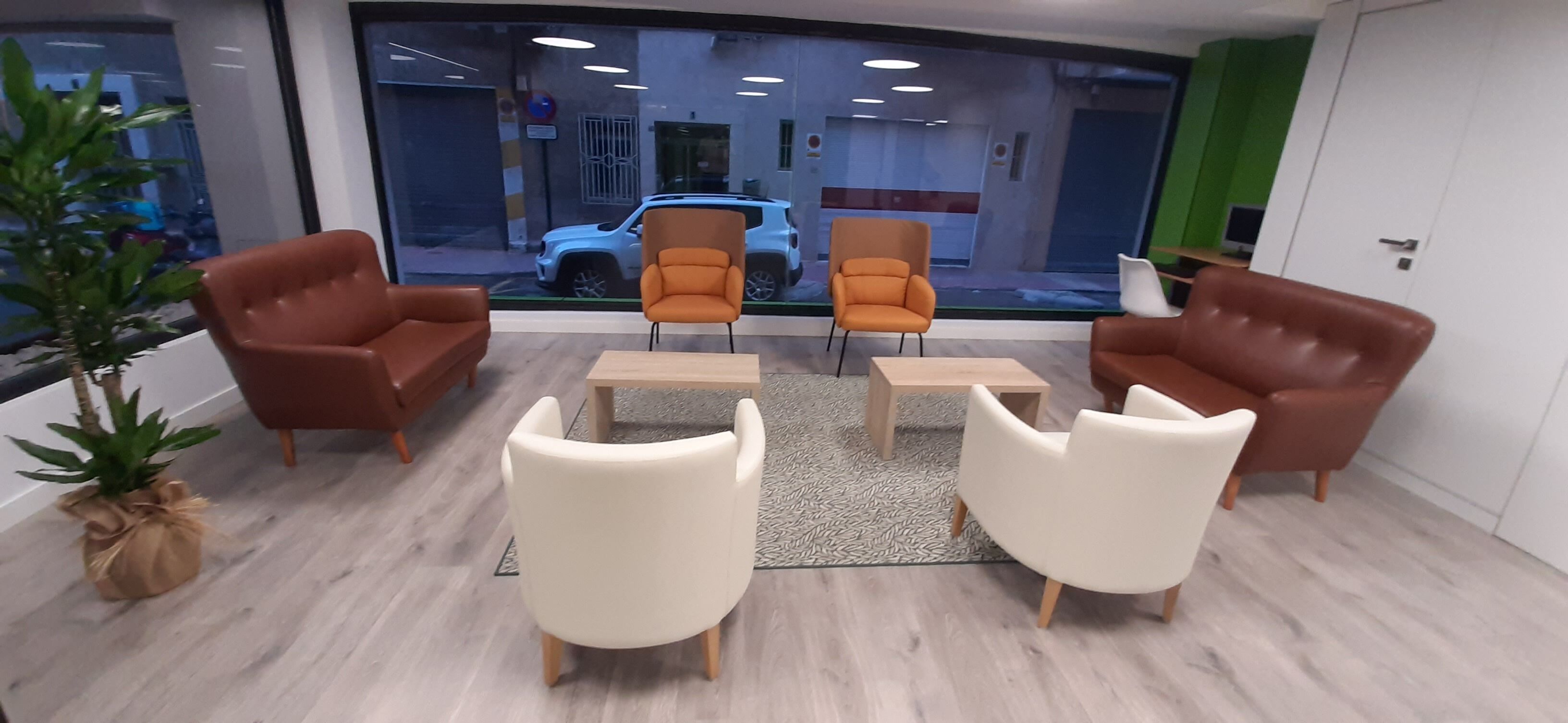 A modern office space with leather chairs, a coffee table, and a view of a parked car outside.