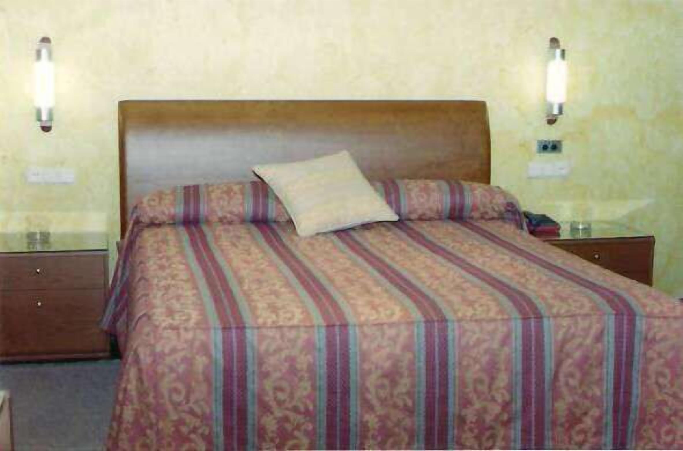 Una habitación de hotel estándar con una cama individual, un cabecero de madera y dos lámparas de noche.