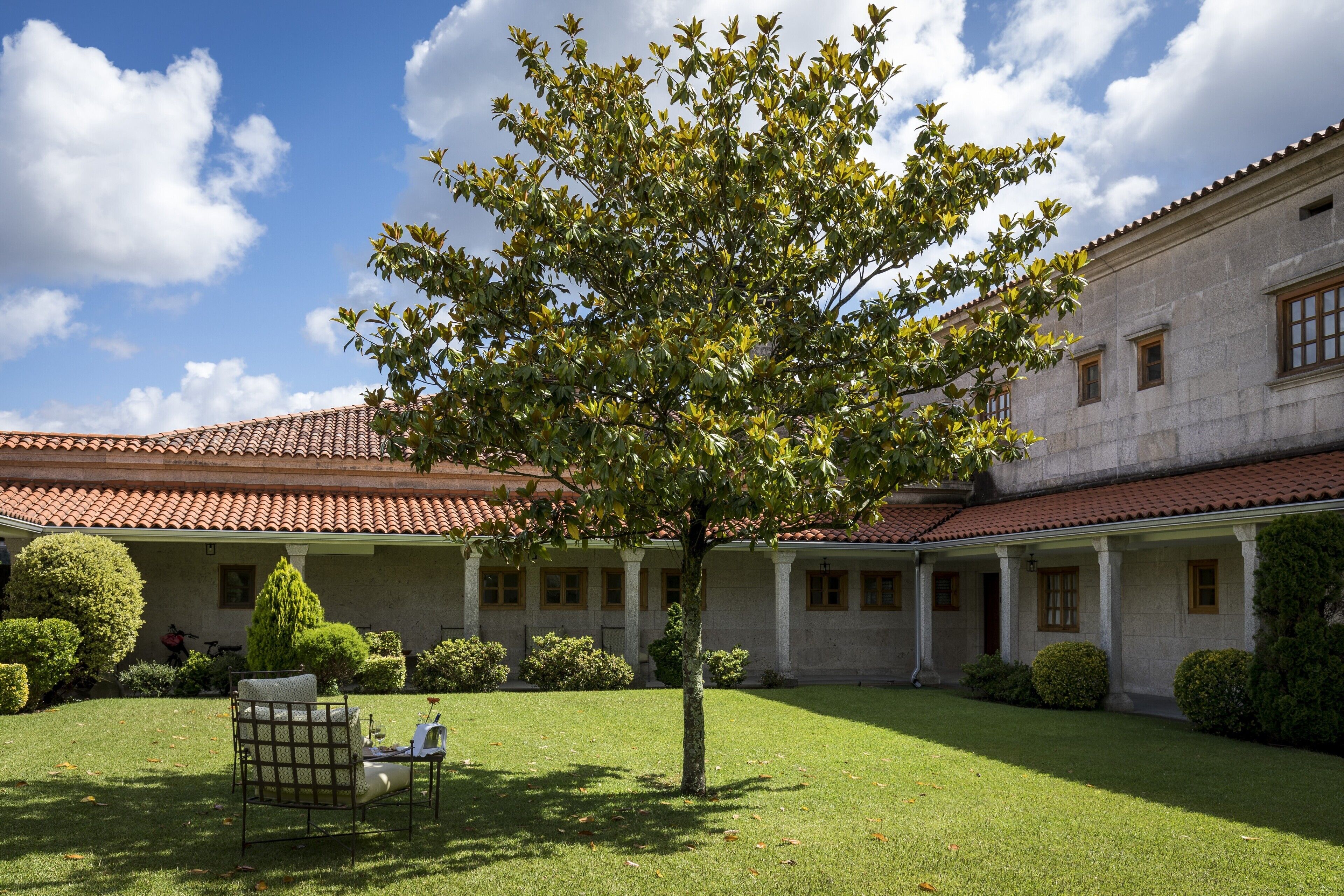 Un patio con un árbol, una banca y un edificio de techo con tejas.