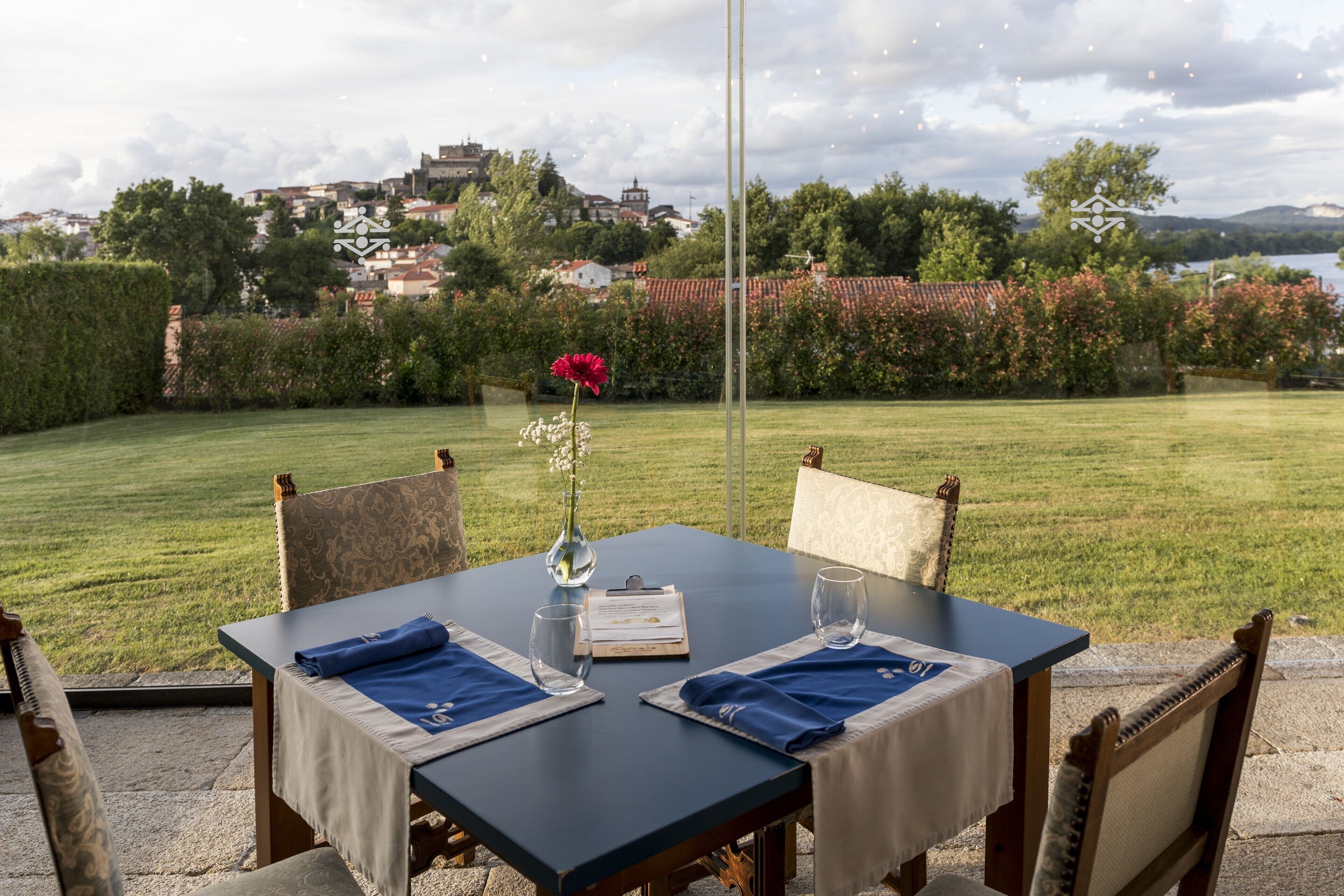 Mesa de comedor al aire libre con vistas a un jardín exuberante y edificios lejanos.